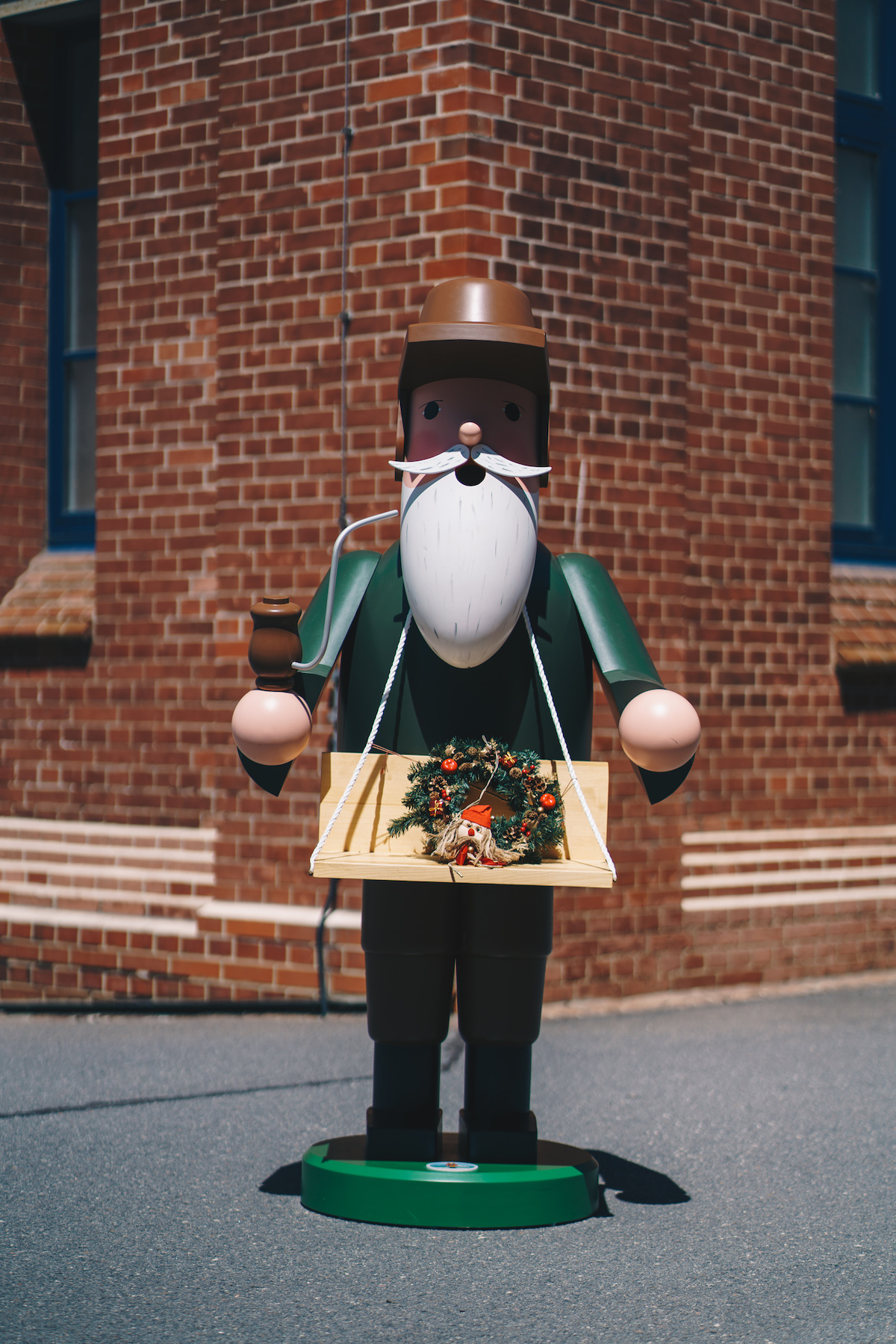A green, life-size wooden smoker stands in front of a brick wall.