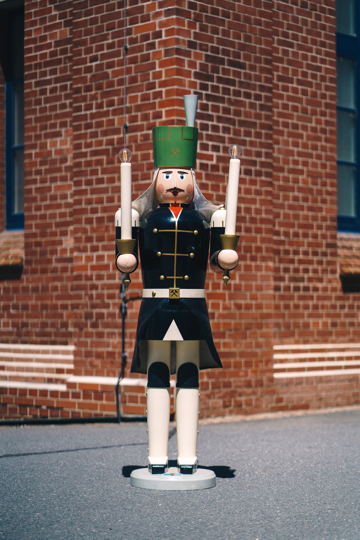 A black and white-green life-size miner made of wood stands in front of a wall made of bricks.