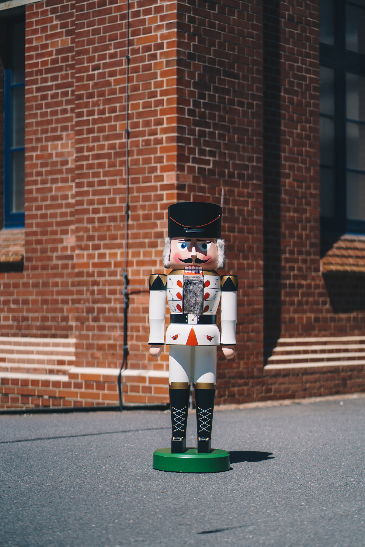 A red life-size nutcracker made of wood stands in front of a wall made of bricks.